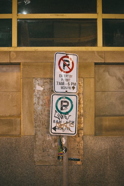 Close-up photograph of a vertically mounted parking restriction sign on a concrete wall at Crystal Palace Park, with a window frame above. The top sign indicates no parking except with a permit between 7 am and 6 pm from Monday to Friday, featuring a red circle with a diagonal line over a 'P' symbol. The lower sign permits parking from 8 am to 6 pm Monday to Friday, with a green circle around a 'P' and an illustration of a hand holding a parking ticket, also mounted on a metal pole. The pole shows signs of wear and has a lanyard or strap hanging from it. The scene is illuminated by ambient lighting, typical of an urban environment, suggesting the signs are part of parking regulation measures relevant during home relocation or furniture transport activities managed by Man with Van Sydenham, which involves logistical planning for moving services.